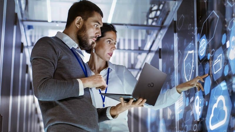 Two IT professionals reviewing data on a laptop in a server room